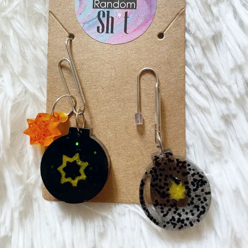 21027-cherry-2 Pendientes únicos con forma de bomba de resina transparente y negra y estrellas de color amarillo y naranja con purpurina.