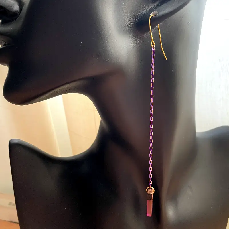 21098-violeta-2 Pendientes extra largos con cadena morada y dorada fina y una pieza rectangular pequeña de madera con resina morada.