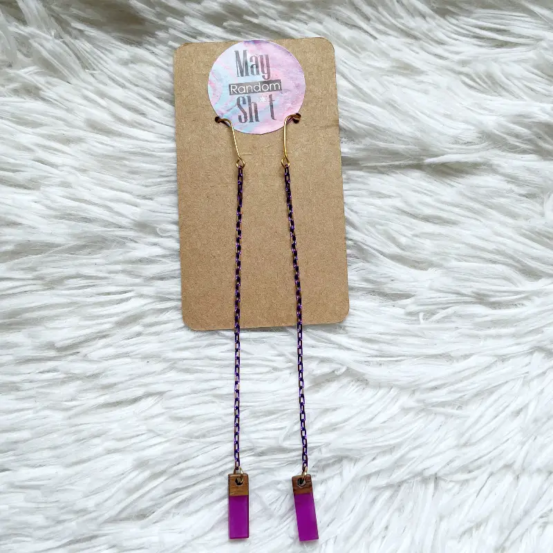 21098-violeta-3 Pendientes extra largos con cadena morada y dorada fina y una pieza rectangular pequeña de madera con resina morada.